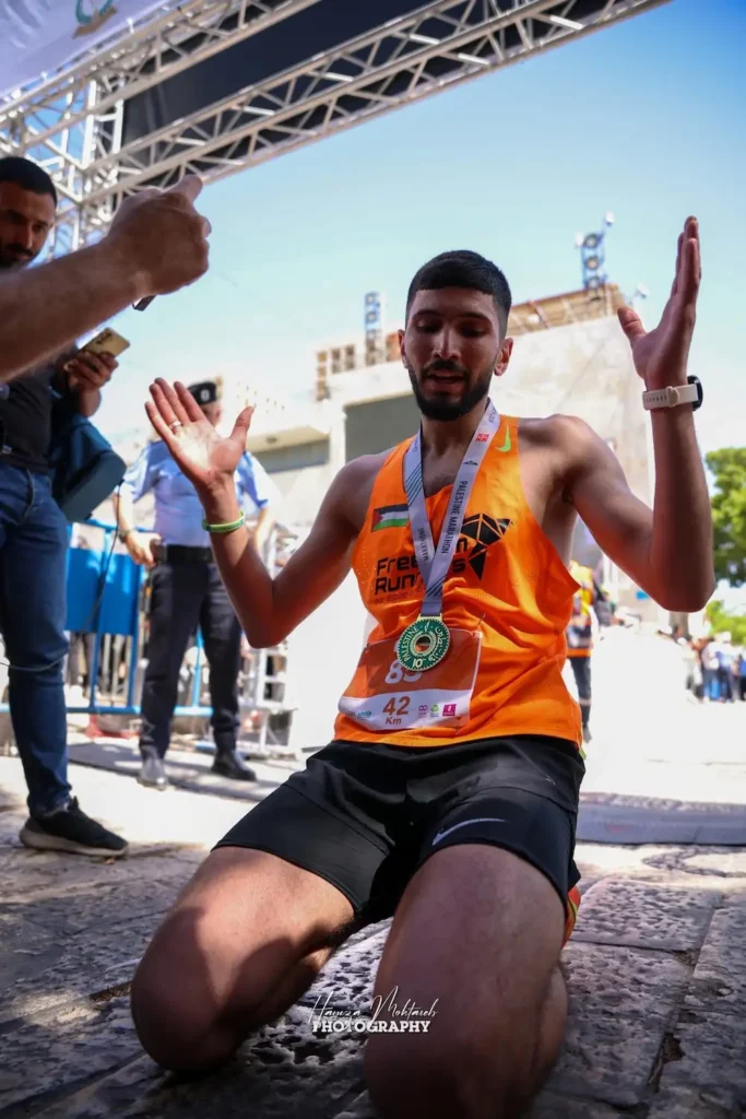 محمد العاصي راكعاً بعد عبور خط النهاية مطوقاً عنقه بميدالية السباق
