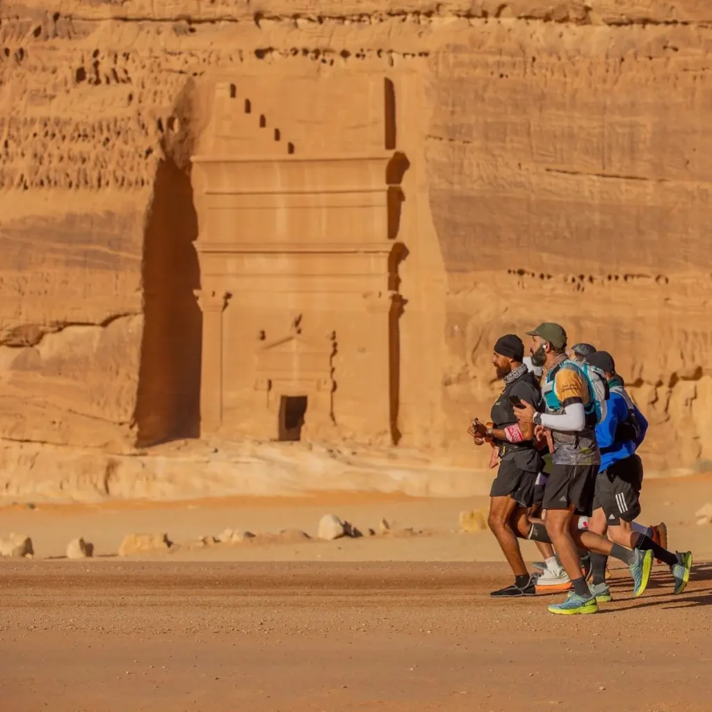 فهد العَبري.. العدّاء العازف بين مجموعة من العدّائين يركضون أمام مقابر أثرية منحوتة في الصخر بمدينة العلا