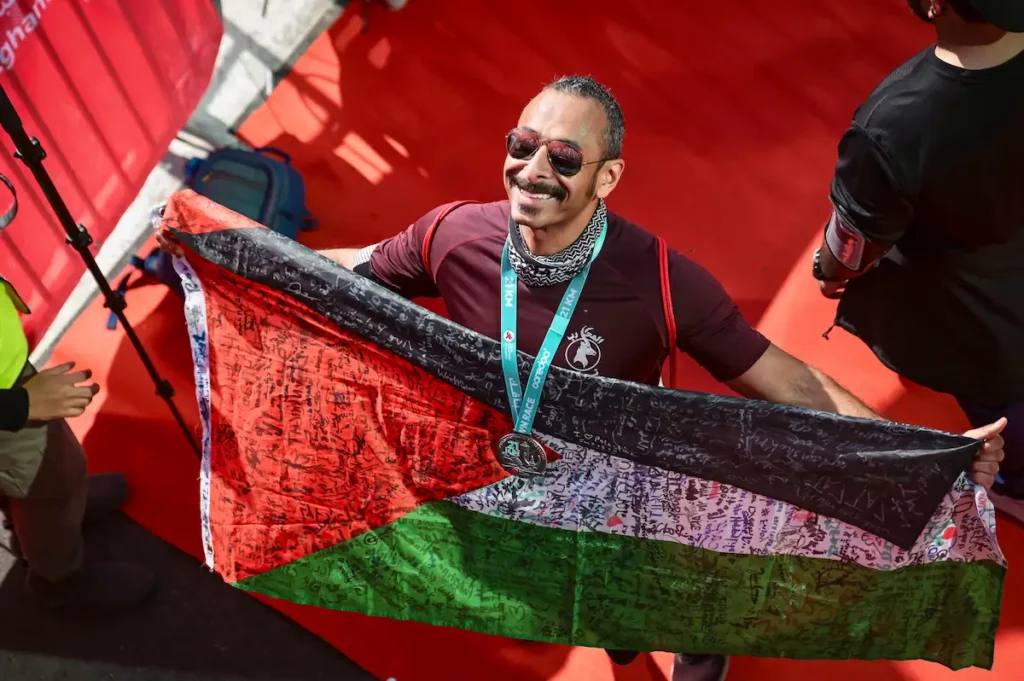 سالم المطوع يحمل العلم الفلسطيني المغطى بتوقيعات عدّائين من مختلف الدول