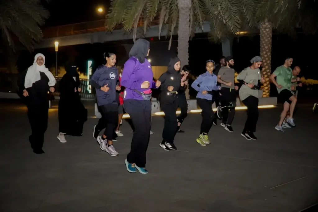 مجموعة من العدّائين، رجالاً ونساءً، يقومون بتمارين الإحماء معاً ليلاً قبل بدء الركض